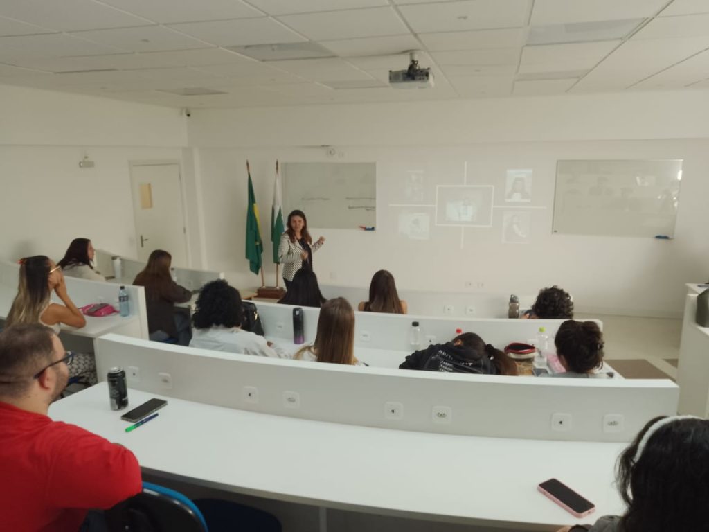 Sala corporativa com a presença dos acadêmicos de psicologia e a docente ministrando palestra